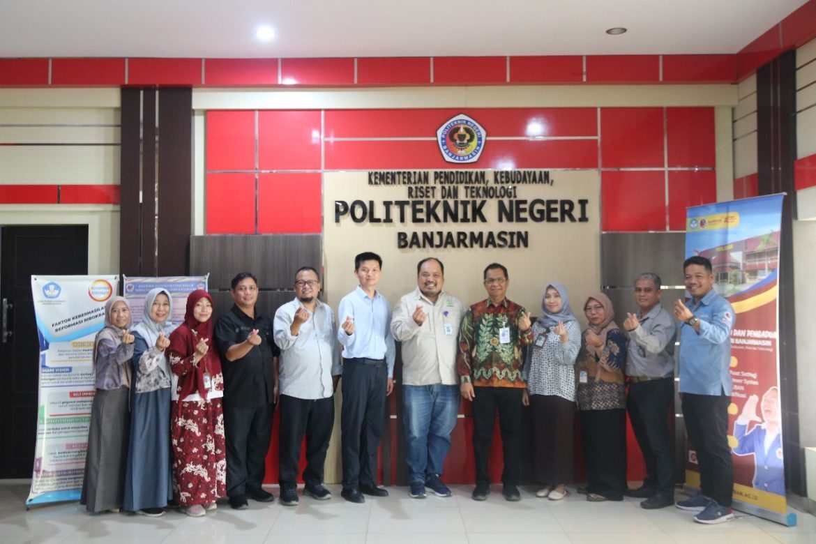Papan nama Politeknik Negeri Banjarmasin di lobi kampus dengan sivitas akademika berfoto bersama di depannya